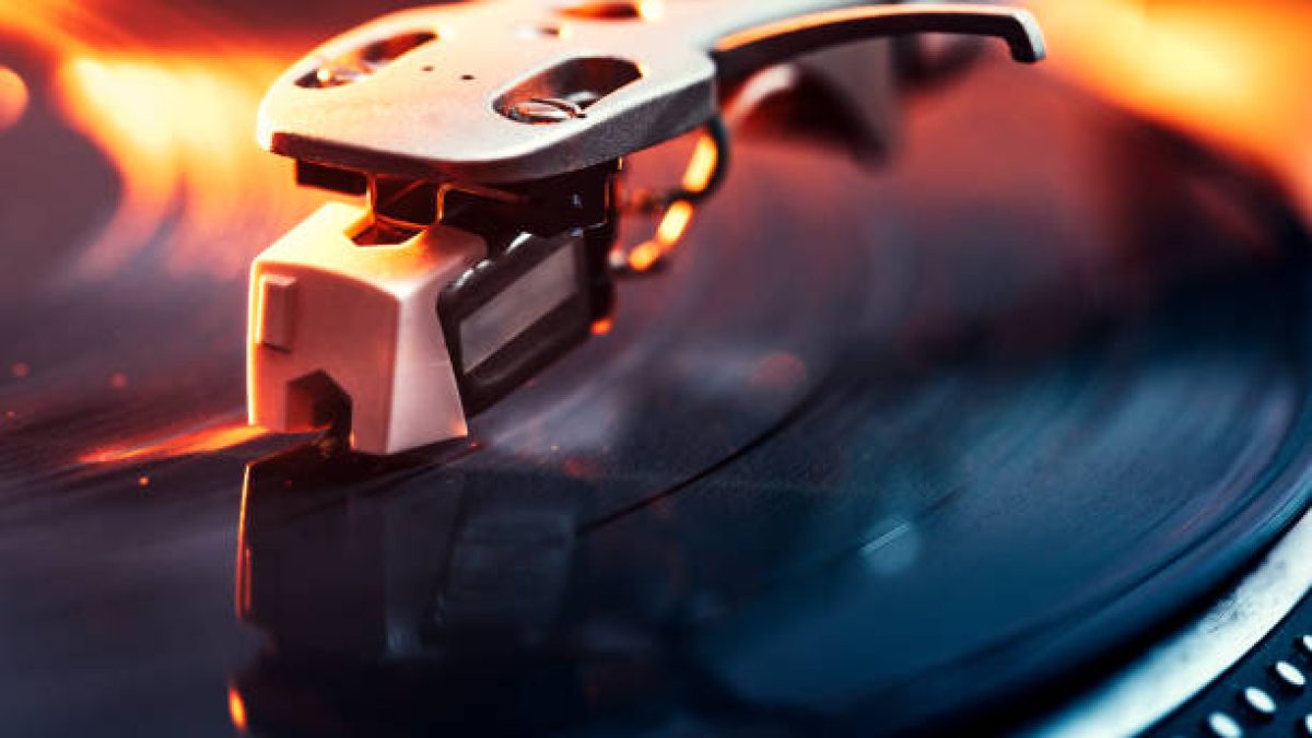 A close up shot of a running record player spinning out some music, dramatically lit with orange light.  Horizontal with copy space.